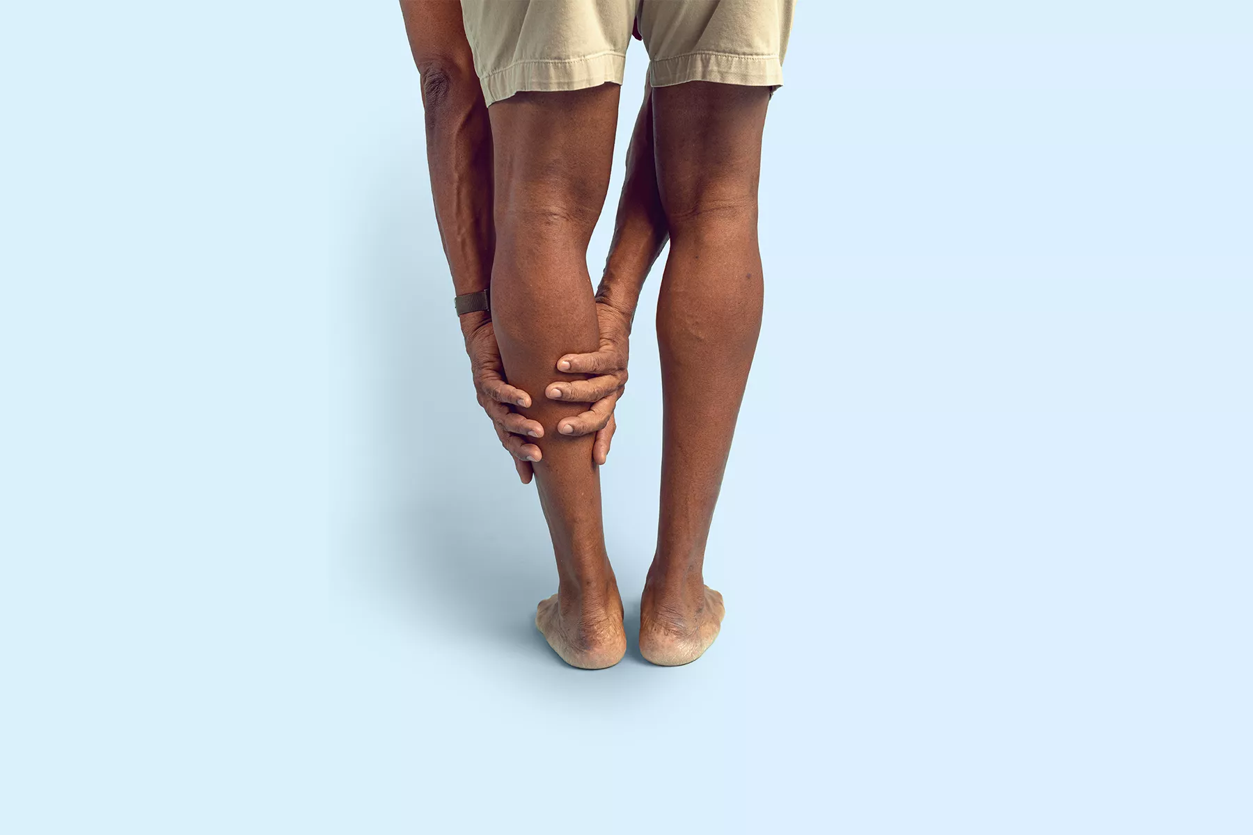 Person bending forward and holding the back of their calf with both hands due to leg pain