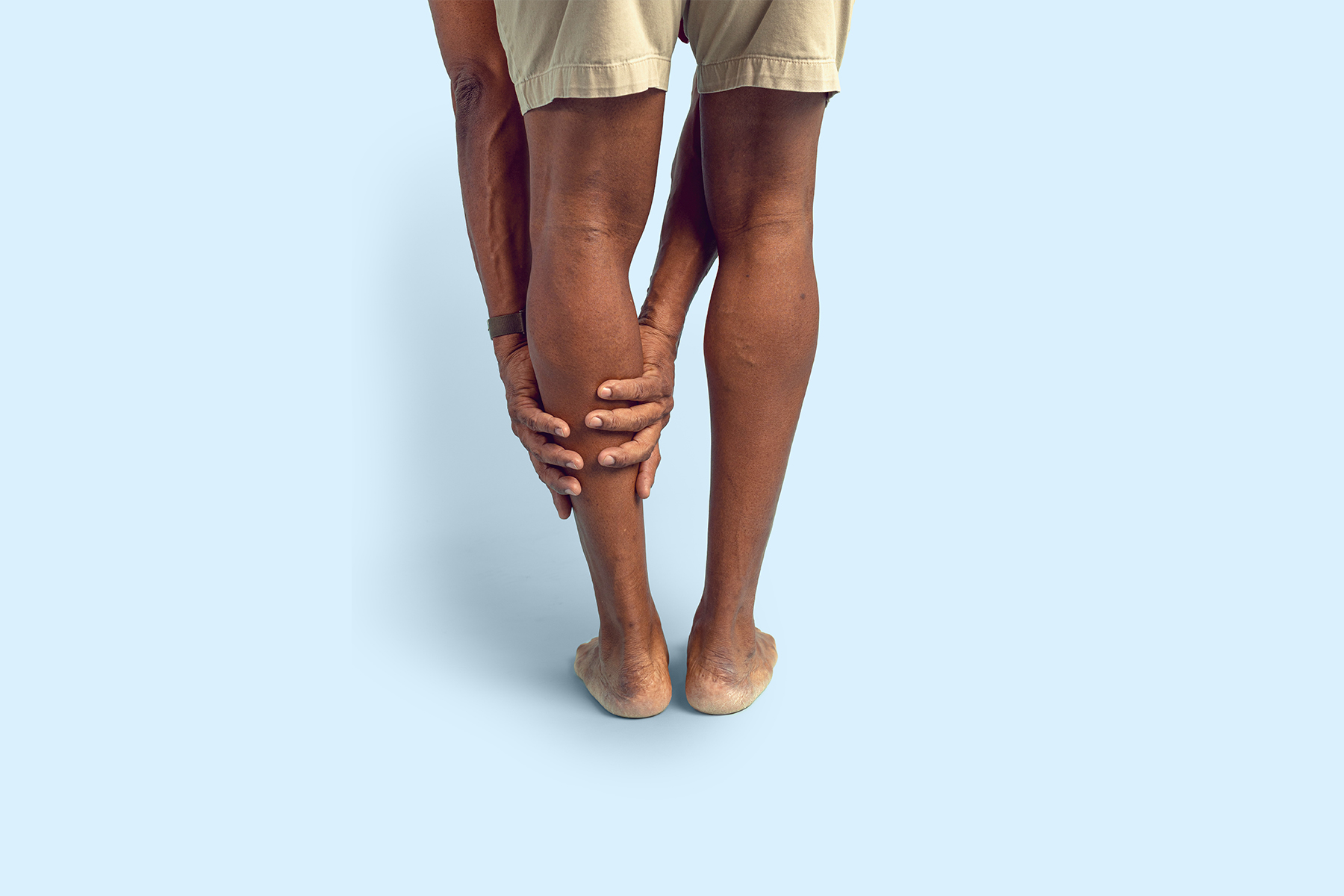 Person bending forward and holding the back of their calf with both hands due to leg pain
